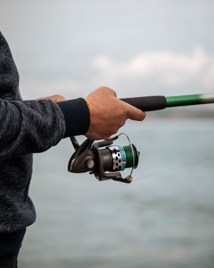 A person in a sweater fishing with a rod over calm waters, evoking tranquility.