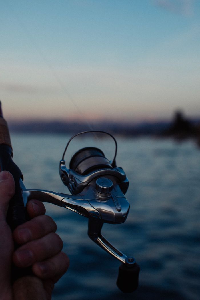 A close-up view of a fishing rod held over a calm lake during dawn, creating a serene atmosphere.
